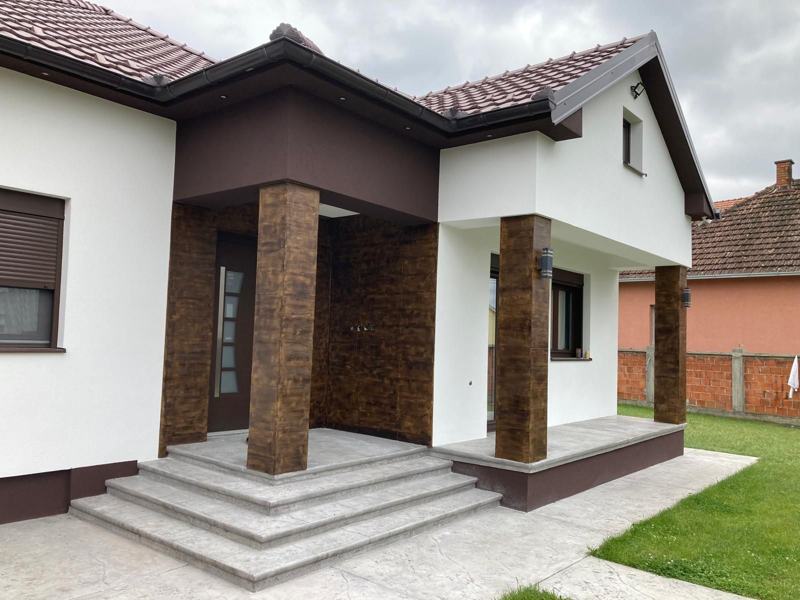 Porodična kuća u Mačvanskoj Mitrovici sa belom fasadom i stubovima u izgledu drveta